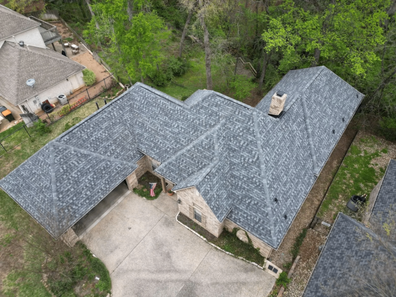 Aerial view of a completed grey architectural shingle roof on a wooded ranch home